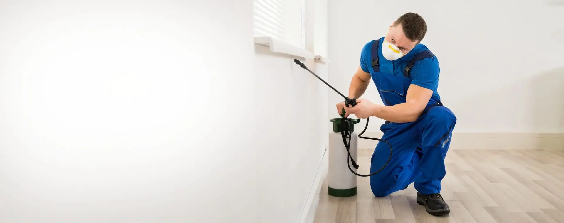 A man in blue shirt spraying water on wall.